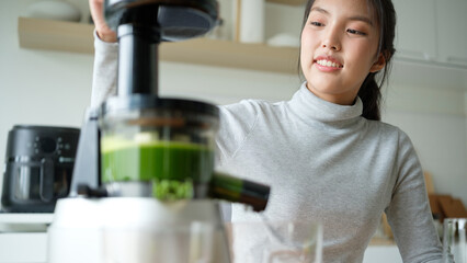 Close-up of a woman using a slow juicer to prepare fresh green vegetable juice in the kitchen.