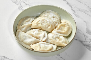 Vareniki or dumplings with potato sprinkled with flour in ceramic bowl on marble table background