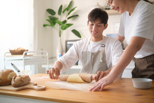 Happy couple enjoying baking at home, flattening dough with a rolling pin.