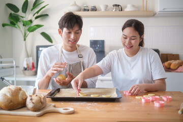 Smiling couple placing cookie dough shapes onto a baking tray in a modern kitchen.