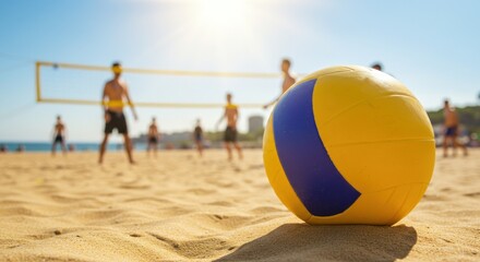 A yellow and blue volleyball sits on a sandy beach with players and a net in the background under a bright sky.