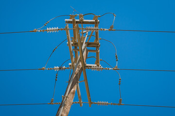 Power line pole with overhead wires for electricity transmission above ground against clear blue sky