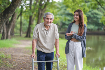 portrait elderly man using walker aid rehabilitation in the park with a young adult daughter take care and support
