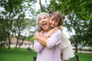 Elderly woman enjoying an affectionate embrace from her young granddaughter during outdoor family...