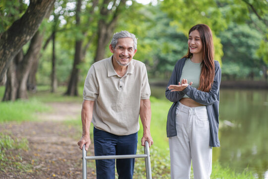 portrait elderly man using walker aid rehabilitation in the park with a young adult daughter take care and support
