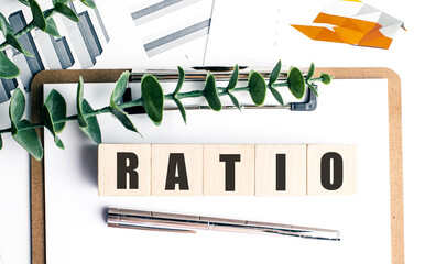 Ratio word on wooden blocks with clipboard, financial charts, pen, and green leaves on white...