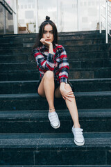 Woman is sitting on a set of stairs in a red and black plaid shirt