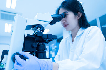 Selective focus woman Asian scientist using microscope to analyze blood smear slide sample at labolatory room.Specialist development and production of new medicines.