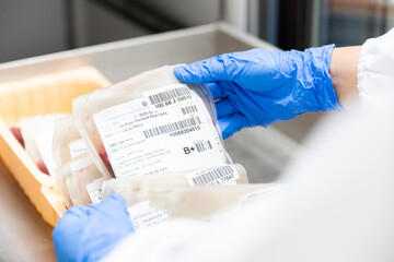 Close up scientist hand wear blue gloves holding red blood bag in storage refrigerator at blood bank unit laboratory.Blood bags received from blood donations used in patients.Save life medical concept