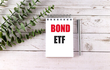 Bond ETF text on spiral notepad with pen and eucalyptus branches on white wooden background