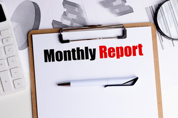 Monthly report text on clipboard with pen, calculator and financial charts on office desk