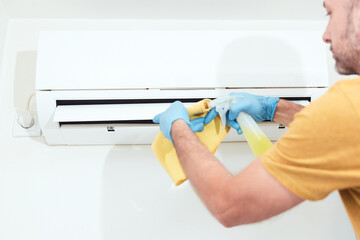 Man cleaning and maintaining air condition unit indoors.