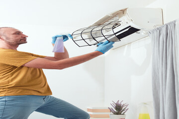 Man cleaning and maintaining air condition unit indoors.