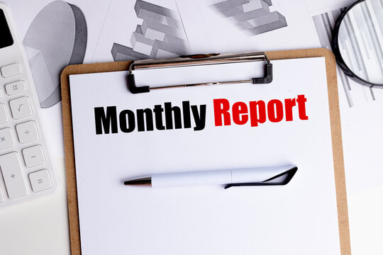 Monthly report text on clipboard with pen, calculator and financial charts on office desk