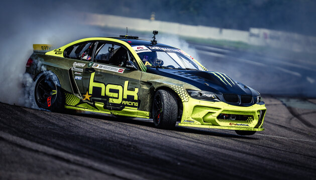 Latvia, Riga, 2025-07-26, Drift Master The image depicts a high-performance race car in action on a track, showcasing its sleek design and powerful engine as it skillfully navigates the curve