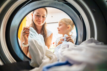 Mother and daughter doing laundry together in a self-service public laundromat, sharing household chores, building responsibility and cooperation in everyday family routine