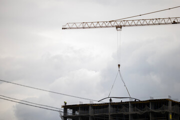 A tower crane lowers steel reinforcement to workers on the top floor of a high-rise construction...
