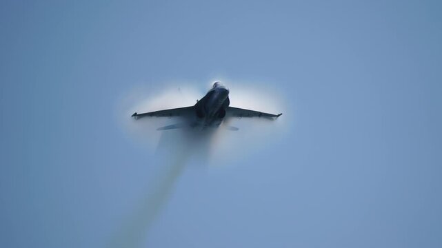 Military jet aircraft flying in slow motion with visible vapor cone from shockwave caused by pressure difference