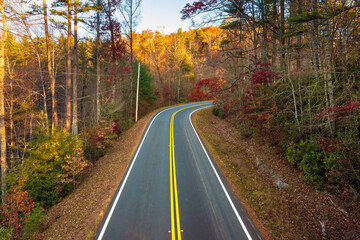 Fototapeta premium Car cruising on scenic road in Appalachian mountains at sunset. Trees glowing in vibrant fall foliage as the sun sets