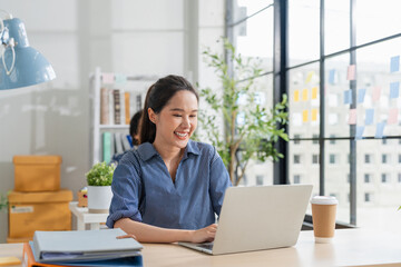 Cheerful Asian businesswoman with positive thinking and confidence sits at her desk, working in a...