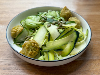 Green salad with falafel, zucchini, cucumbers, and pumpkin seeds. Vegetarian cuisine concept. Handheld mobile photo, selective focus, non AI