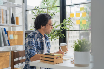 Cheerful Asian businessman with positive thinking and confidence sits at her desk, working in a...