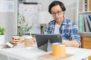 Cheerful Asian businessman with positive thinking and confidence sits at her desk, working in a...