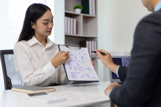 Asian woman attending job interview and showing resume to hr manager, talking about her profile and experience for job opportunity in office.
