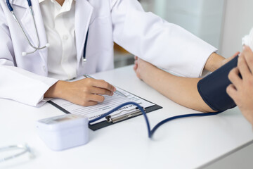 Female doctor measuring blood pressure of patient in hospital room. Doctor using sphygmomanometer...