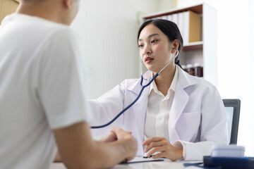 Female doctor examining patient with stethoscope in hospital room. Asian female doctor using...