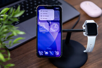 Poznan, Poland - July 29, 2025: Apple iPhone and Watch featuring ios 26 interface with Liquid Glass, on a stand, highlighting modern tech and smart home connectivity