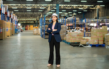 A confident female supervisor in a suit and hard hat inspects stocked shelves in a large warehouse.