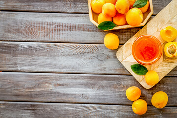 Summer preserves. Apricot jam in jar near fresh fruits on dark wooden background top view frame...