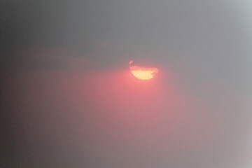 Dramatic sun breaking through heavy overcast clouds creating ethereal orange and pink glow in moody atmospheric sky during stormy weather conditions