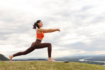 Athletic middle aged blonde woman standing in warrior pose on fitness mat, sporty lady practicing...