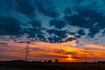 Summer sunset or sundowner view with a dramatic sky and overland high voltage lines near Tabertshausen, Aholming, Deggendorf, Bavaria, Germany