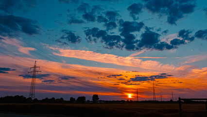 Summer sunset or sundowner view with a dramatic sky and overland high voltage lines near Tabertshausen, Aholming, Deggendorf, Bavaria, Germany