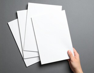 Top view of a hand holding blank white A4 paper sheets on gray background.