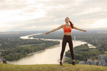 Excited lady in sportswear enjoying nature and beautiful view after successful fitness training outdoors in mountains, woman feeling free with open arms