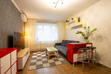 Apartment interior. Living room with furniture: dark gray sofa, red chest of drawers, metal chairs,...
