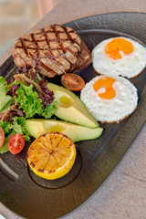 Grilled Steak with Fried Eggs, Fresh Salad, Avocado Slices, and Grilled Lemon on a Plate for a Delicious and Nutritious Breakfast Experience