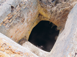  Abandoned stone and brick well with dry grass around and dark water inside, creating a mysterious...