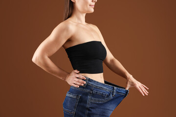 Fit woman wearing old jeans after weight loss on brown background, closeup