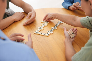 Friends playing dominoes at wooden table, closeup