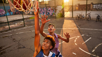 Urban streetball action: teenagers play basketball on an outdoor court. Friends in competition at sunset, player scores a slam dunk.