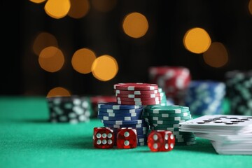Casino chips, dice and playing cards on green table against blurred lights, closeup