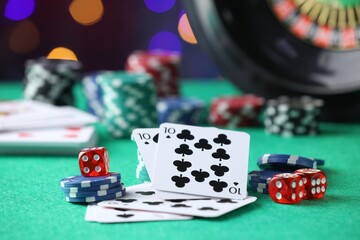 Casino chips, dice and playing cards on green table against blurred lights, closeup