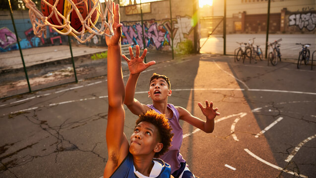 Urban streetball action: teenagers play basketball on an outdoor court. Friends in competition at sunset, player scores a slam dunk.