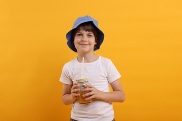 Cute little boy in panama hat with mason jar of juice on orange background. Refreshing drink