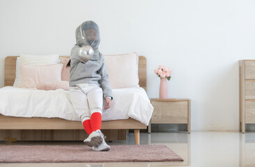 A girl in fencing gear is sitting and rest on the bed